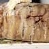 A block of aged cheese with a textured surface placed on a wooden board. - Olive Oil Times