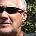 Man with short gray hair wearing sunglasses, with olive trees in the background. - Olive Oil Times