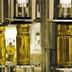 Three glass bottles filled with olive oil being processed on a bottling line. - Olive Oil Times