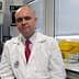 A man wearing a lab coat and a red tie sitting in a laboratory environment. - Olive Oil Times