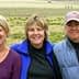 Three women standing together outdoors, smiling at the camera with a grassy background. - Olive Oil Times
