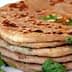 A stack of paratha bread garnished with fresh cilantro leaves on a white plate. - Olive Oil Times