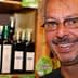 Man with glasses smiling in front of shelves displaying olive oil bottles. - Olive Oil Times