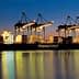 A large container ship named Hapag-Lloyd docked at a port with cranes illuminated at dusk. - Olive Oil Times