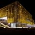 Contemporary building featuring a yellow facade with a textured surface, illuminated at night. - Olive Oil Times