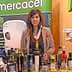 Woman standing behind a table with various bottles of olive oil at an exhibition booth. - Olive Oil Times