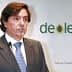 Man in a suit speaking at a presentation with Deoleo logo in the background. - Olive Oil Times