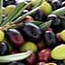 A mix of green, black, and purple olives with olive leaves scattered among them. - Olive Oil Times