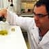Scientist in a lab coat pouring olive oil from a bottle into a beaker in a laboratory setting. - Olive Oil Times