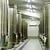 Row of stainless steel storage tanks in an industrial facility with pipes and valves. - Olive Oil Times