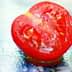 A halved tomato showing its interior with seeds and flesh visible on a reflective surface. - Olive Oil Times