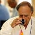 An older man in a white shirt tasting olive oil from a small glass cup. - Olive Oil Times