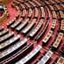 Interior view of the Greek Parliament chamber featuring rows of wooden seating and a red carpet. - Olive Oil Times