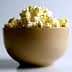 A beige bowl filled with freshly popped popcorn against a plain background. - Olive Oil Times
