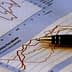 A pen resting on a sheet of paper with financial graphs and data trends. - Olive Oil Times