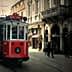 A red vintage tram traveling along a street in Istanbul with pedestrians nearby. - Olive Oil Times