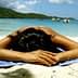 Individual lying face down on a beach towel on a sandy beach near the water. - Olive Oil Times
