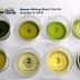 Eight small cups containing different olive oil samples labeled with numbers on a white sheet. - Olive Oil Times