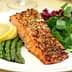 Grilled salmon fillet served with asparagus, lemon slices, and mixed salad greens on a white plate. - Olive Oil Times