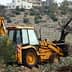 Yellow backhoe loader working in an olive grove, with an olive tree in the background. - Olive Oil Times