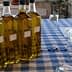 Four bottles of olive oil arranged on a checkered tablecloth with glasses nearby. - Olive Oil Times