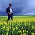 A man holding a flower while standing in a field of yellow flowers under a cloudy sky. - Olive Oil Times