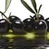 A cluster of black olives resting in olive oil with a reflective surface. - Olive Oil Times