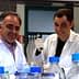 Two male scientists wearing lab coats and gloves working with laboratory equipment and bottles. - Olive Oil Times