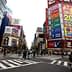 A busy intersection in Tokyo featuring large advertisements and pedestrians crossing the street. - Olive Oil Times
