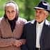 Elderly couple holding hands while walking outdoors, dressed in traditional clothing. - Olive Oil Times