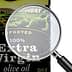 Bottle of extra virgin olive oil with a magnifying glass focusing on the label details. - Olive Oil Times