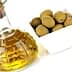 A glass bottle of olive oil with a cork stopper next to a bowl of green olives. - Olive Oil Times