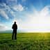 Silhouette of a person standing on a green field with a blue sky and clouds in the background. - Olive Oil Times