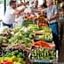 Vendors and customers interacting at a fresh produce market with various vegetables displayed. - Olive Oil Times