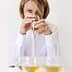 Woman holding a glass of olive oil while tasting it, with several glasses in front of her. - Olive Oil Times