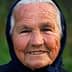 Elderly woman with a warm smile, wearing a dark headscarf and showing facial wrinkles. - Olive Oil Times
