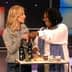 Two women interacting while presenting various olive oil products on a table. - Olive Oil Times