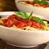 Bowl of spaghetti topped with tomato sauce and fresh basil leaves. - Olive Oil Times