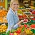 Woman in a gray blazer holding a red apple while carrying a basket of fresh fruits and vegetables. - Olive Oil Times
