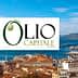 Logo of Olio Capitale Expo displayed over a coastal city view with boats and buildings. - Olive Oil Times
