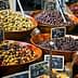 Multiple wooden bowls filled with different types of olives displayed at a market. - Olive Oil Times