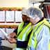 Two workers in safety vests and hairnets examining a document in a workplace setting. - Olive Oil Times