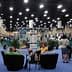 Exhibition hall with attendees seated in chairs and various displays in the background. - Olive Oil Times