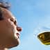 A man examining a glass of olive oil against a blue sky background. - Olive Oil Times