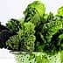 A colander filled with various green leafy vegetables including kale, spinach, and herbs. - Olive Oil Times