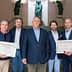 Five individuals posing together at an event, holding certificates in front of a sculpture backdrop. - Olive Oil Times