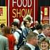 Crowd of attendees at a food show event with a large red banner in the background. - Olive Oil Times