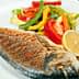 Grilled fish served with a side of colorful sautéed vegetables and lemon slices on a white plate. - Olive Oil Times