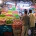 Two individuals observing a fruit stall filled with various types of apples and other fruits in baskets. - Olive Oil Times