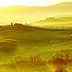 Rolling hills of Tuscany with cypress trees and a farmhouse under a golden sunset. - Olive Oil Times